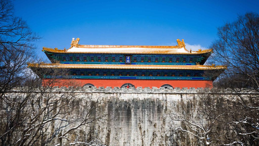 Photo of Chinese Palace behind an old large stone wall in blue sky.