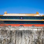 Photo of Chinese Palace behind an old large stone wall in blue sky.